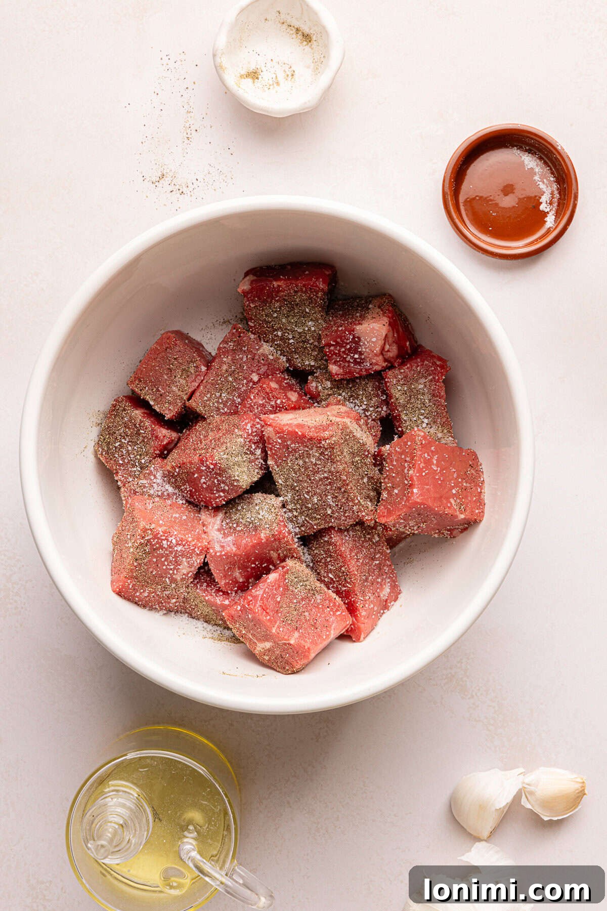 raw steak bites in a bowl with salt and pepper surrounded by ingredients