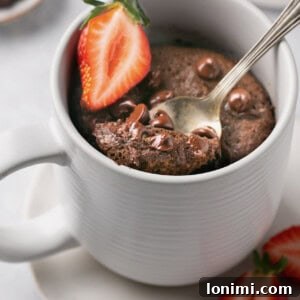 protein chocolate mug cake topped with chocolate chips and a strawberry slice with a spoonful being taken out