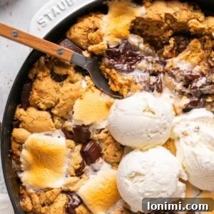 chocolate and marshmallow smores cookie skillet topped with ice cream with a spoon taking a bite