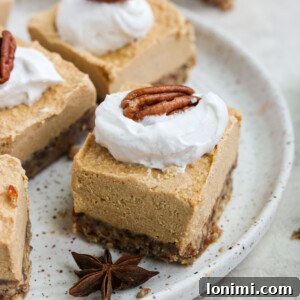 Paleo Vegan Pumpkin Cheesecake square with whipped cream and a pecan on a plate