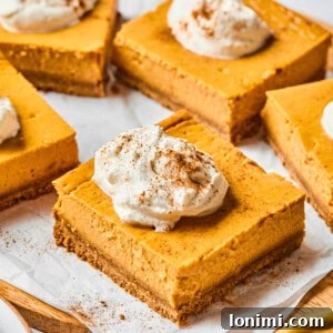 pumpkin cheesecake bars on parchment with whipped cream