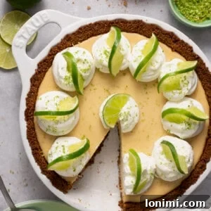 Gluten free key lime pie in a white Staub pie plate surrounded by ingredients with a slice taken out