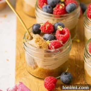 no bake mini cheesecakes in glass jars topped with berries with a spoon taking a bite