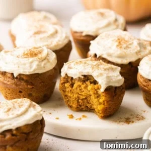pumpkin muffins topped with cream cheese frosting and one has a bite taken out of it