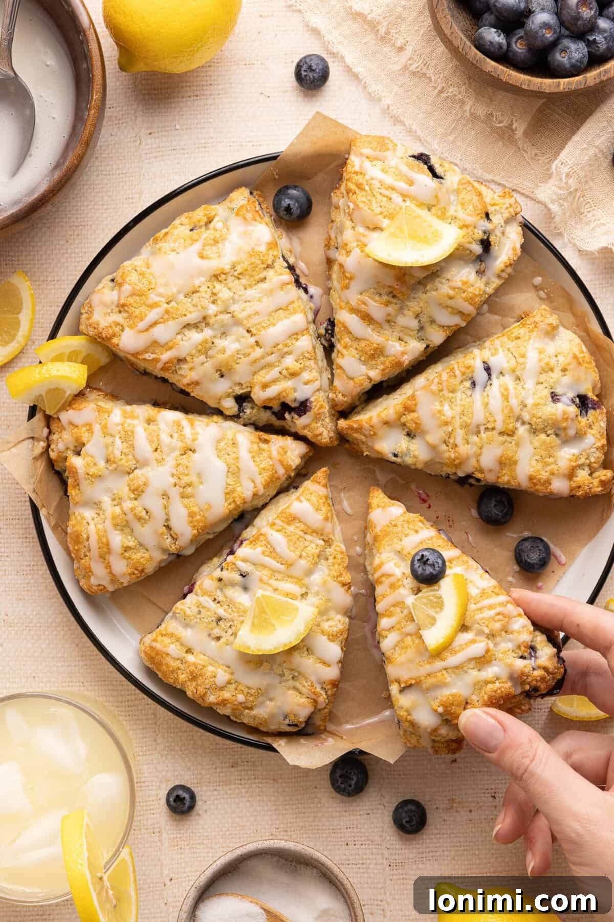 Effortless Gluten Free Blueberry Lemonade Scones 2 8 blueberry lemonade scones on a plate with lemon slices and a hand holding one