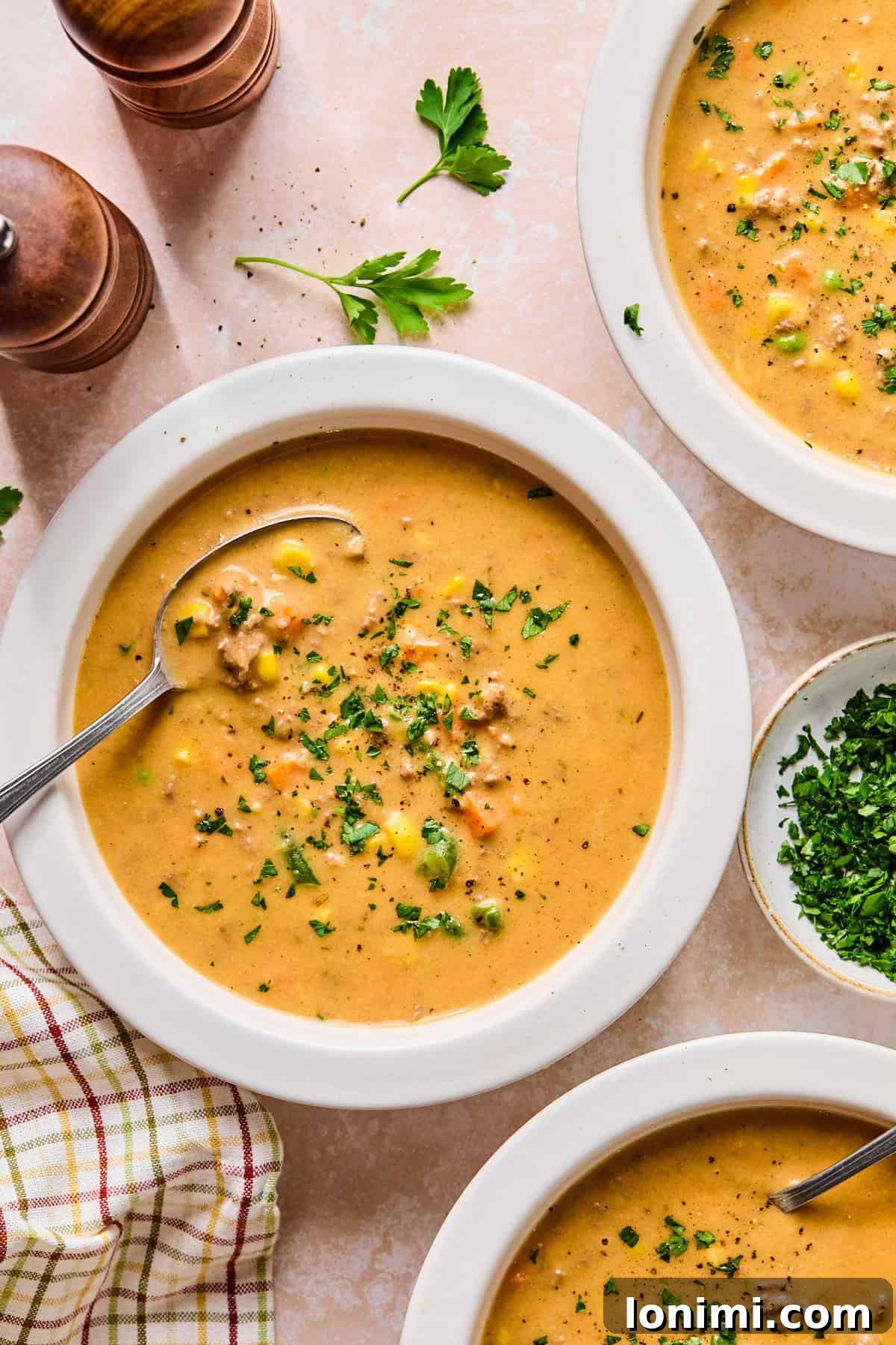 Two inviting bowls of shepherd’s pie soup arranged on a light pink countertop, accompanied by fresh parsley for garnish.