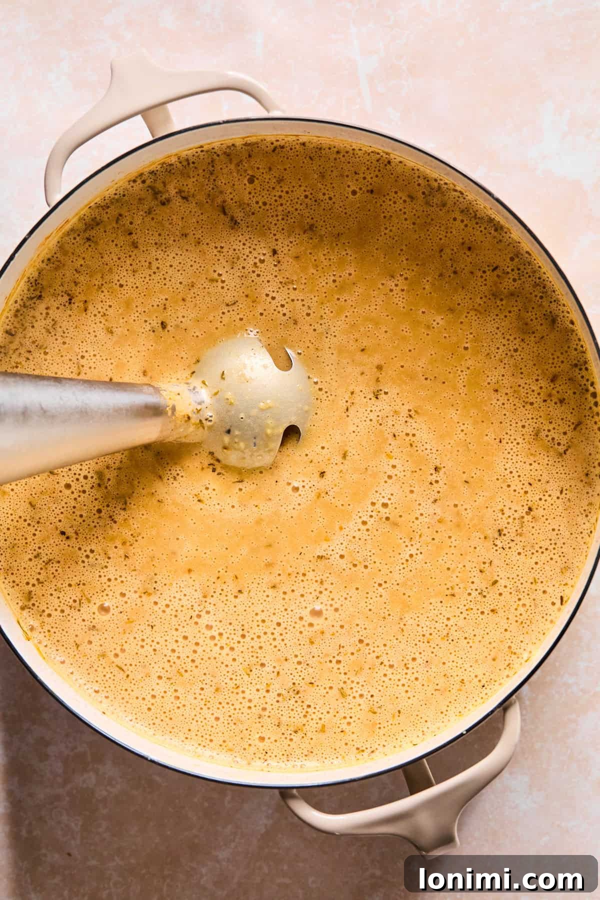 Blending the soup base with an immersion blender to achieve a creamy, smooth texture.