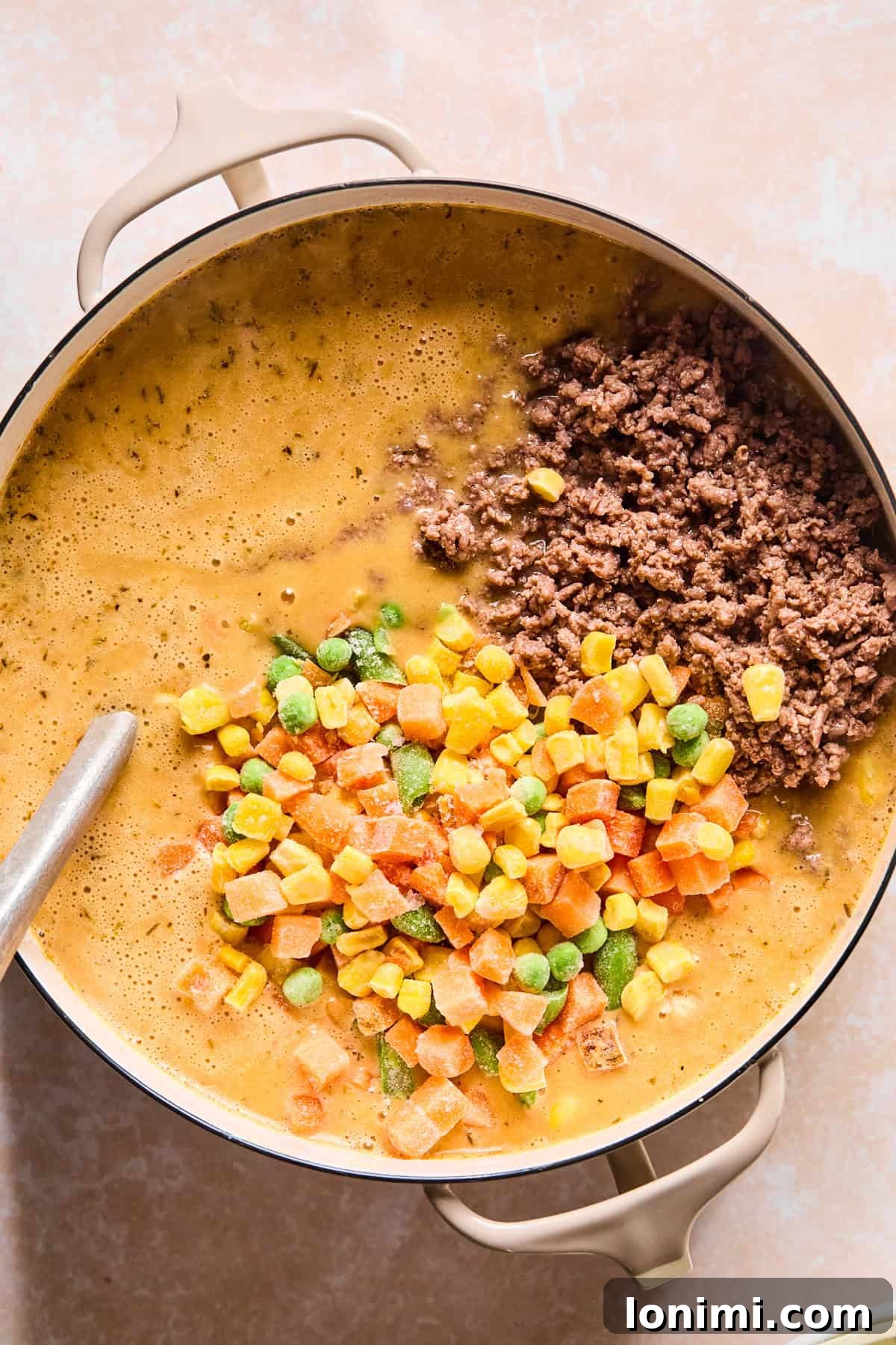 Stirring cooked ground beef and frozen mixed vegetables back into the shepherd's pie soup.