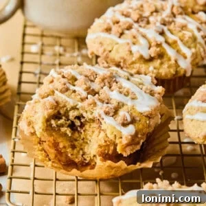 A close-up of a coffee cake muffin on a cooling rack with a bite taken out, revealing its fluffy interior and cinnamon swirl.