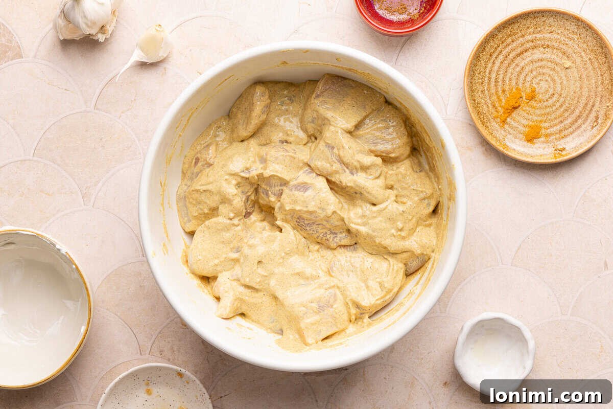 Chicken cubes marinating in a creamy yellow yogurt and spice mixture in a glass bowl.