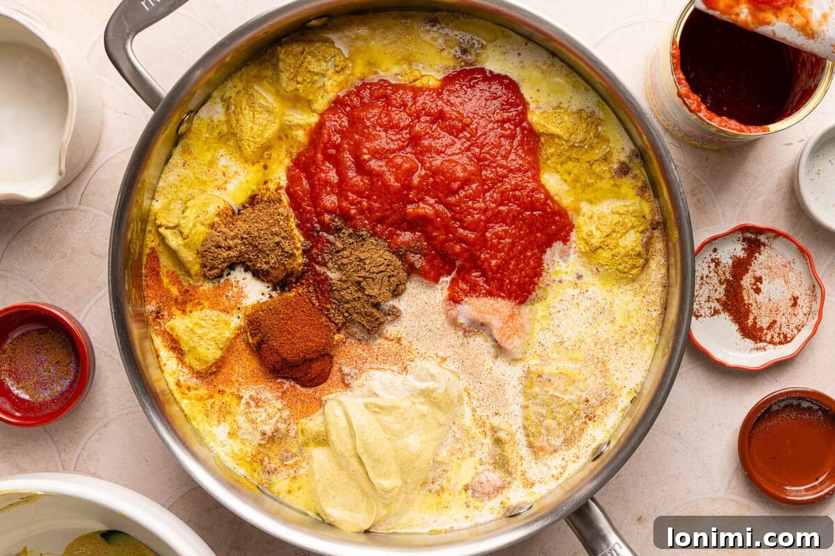 A pan filled with seared chicken, creamy tomato sauce, and various spices being combined.