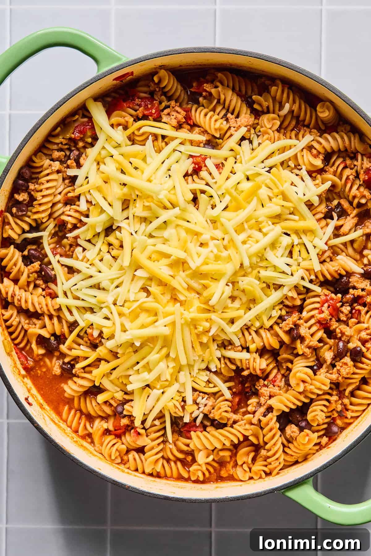 Easy Gluten-Free One Pot Taco Pasta 8 Shredded cheese being stirred into one pot taco pasta until melted and creamy.