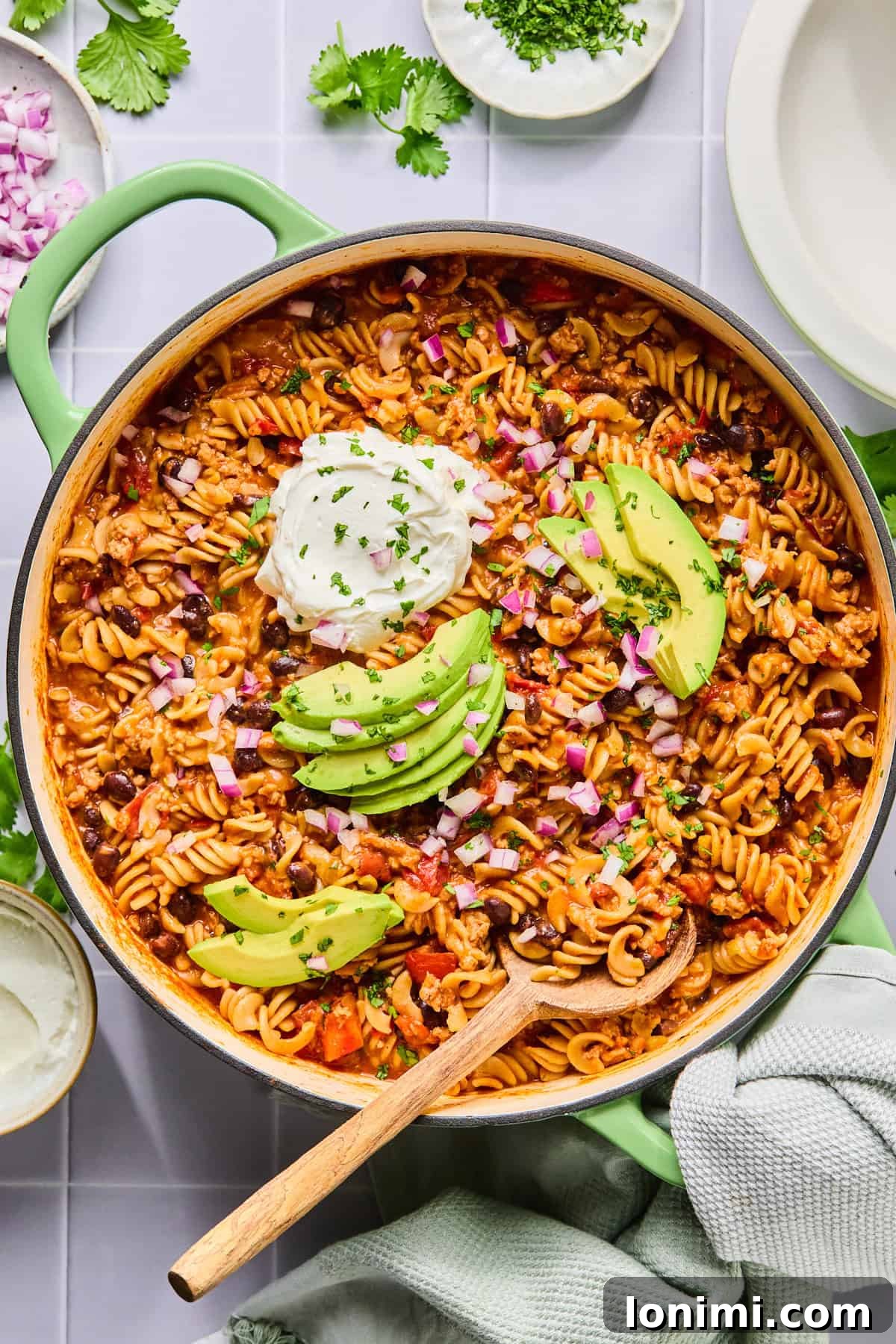 Easy Gluten-Free One Pot Taco Pasta 9 One pot taco pasta in the pot topped with sour cream, avocado, and cilantro with a wooden spoon.