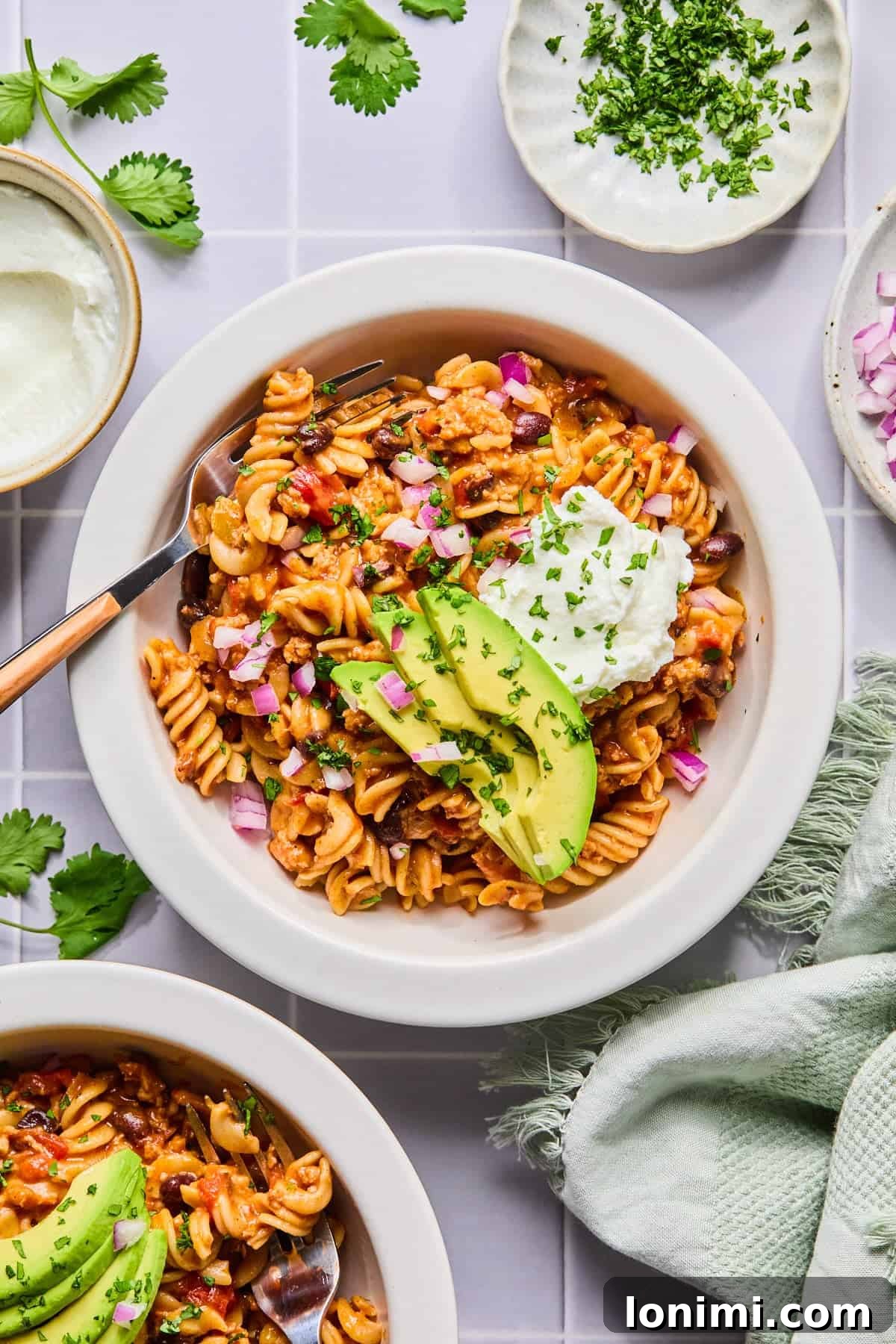 Easy Gluten-Free One Pot Taco Pasta 10 Bowl of one pot taco pasta garnished with sour cream, avocado, and cilantro with a fork.