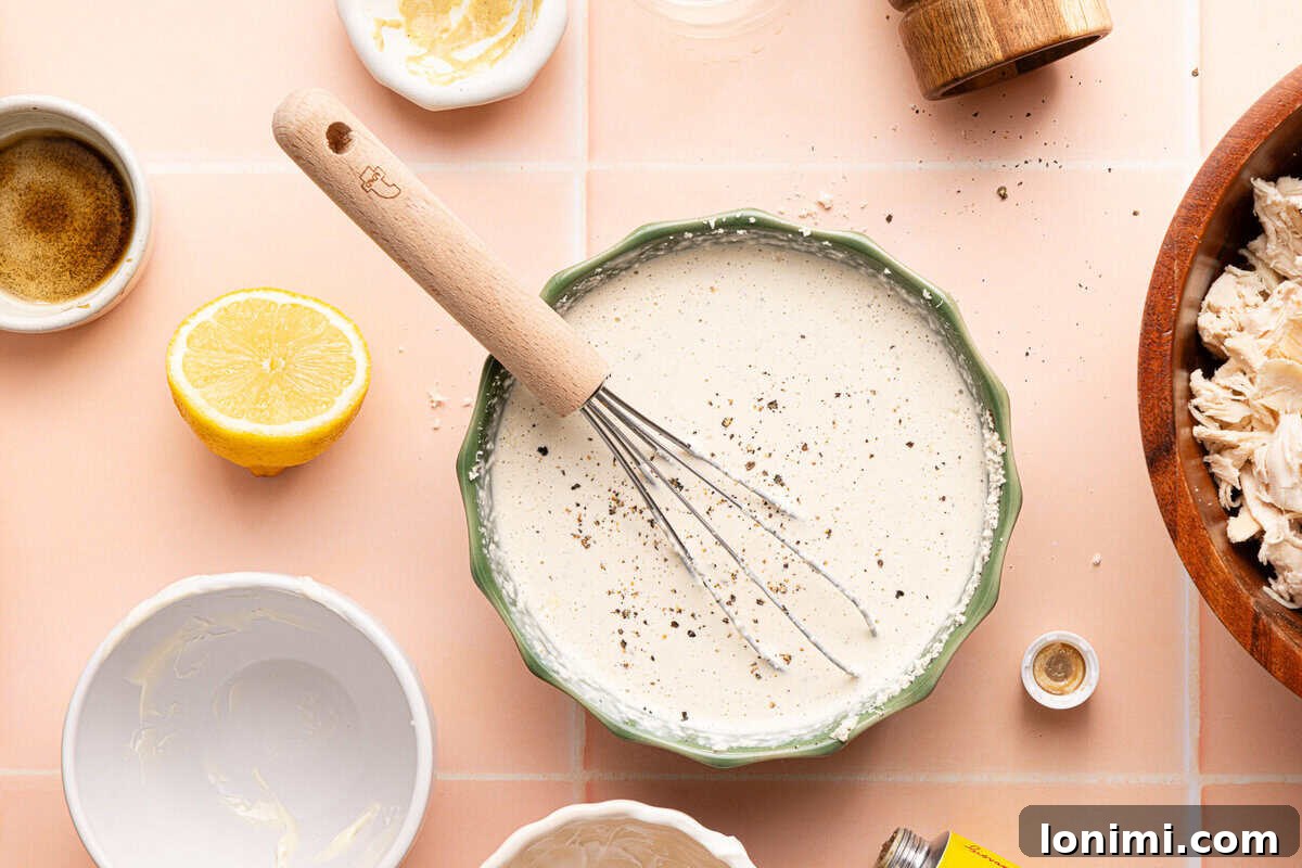homemade caesar dressing in a bowl with a whisk surrounded by ingredients