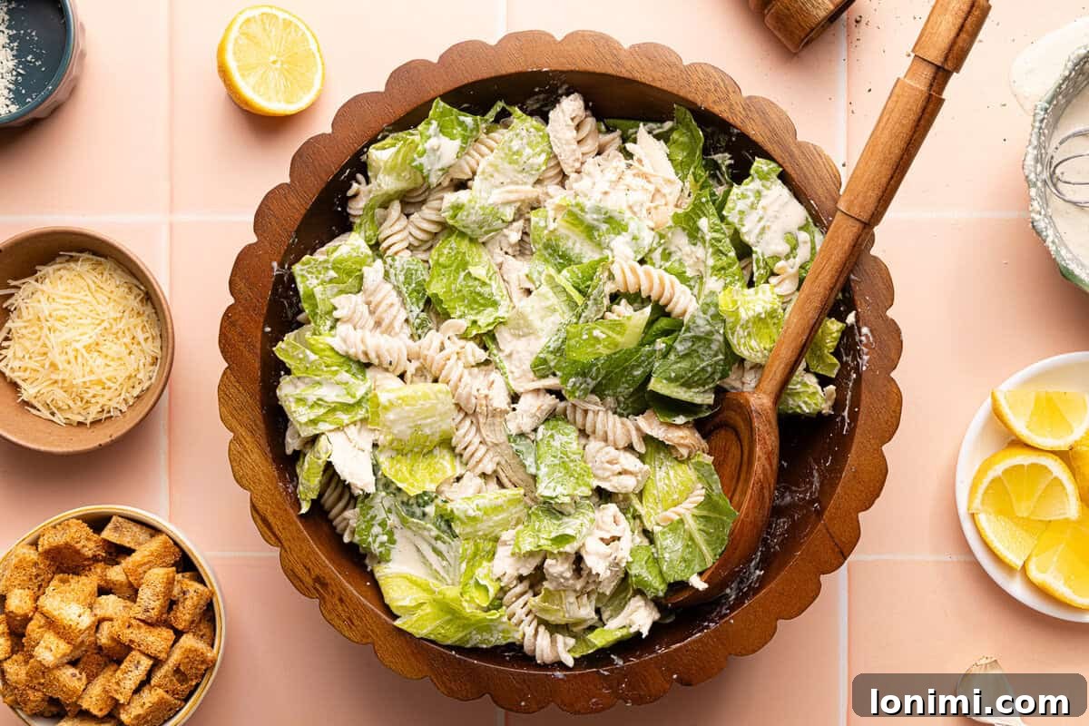 chicken caesar pasta salad tossed together in a wooden bowl with a wooden spoon