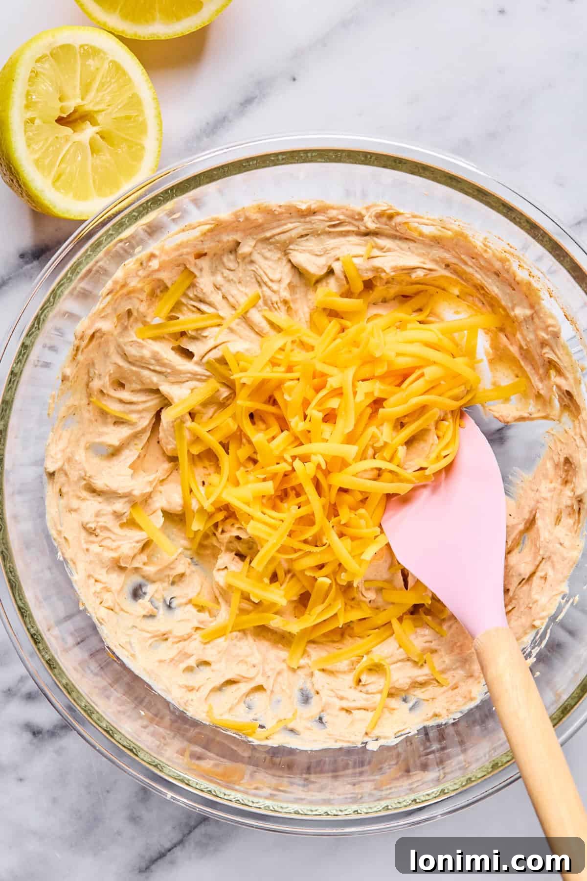 Ultimate Creamy Crab Dip Warm or Cold 5 Shredded cheddar cheese being folded into the creamy crab dip mixture.