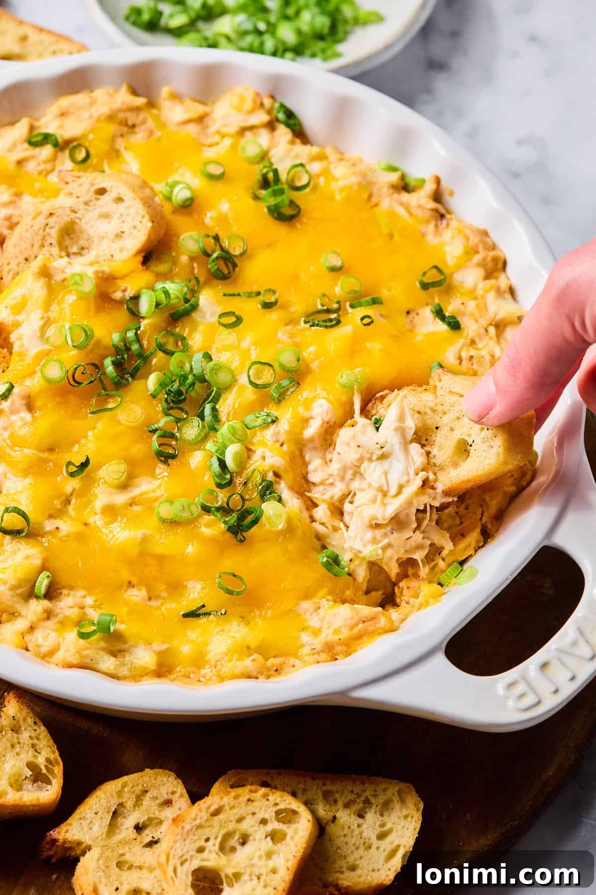 Ultimate Creamy Crab Dip Warm or Cold 9 Baguette slice being dipped into warm, creamy crab dip.