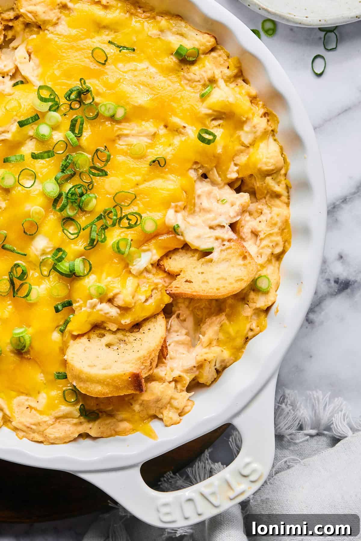 Ultimate Creamy Crab Dip Warm or Cold 10 Close-up of hot crab dip in a baking dish garnished with green onions and served with baguette slices.