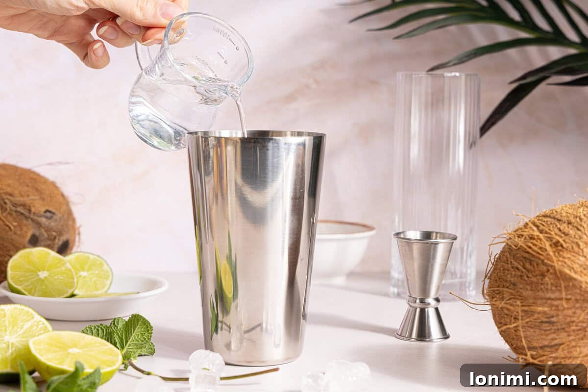 White rum being poured into a cocktail shaker filled with ice