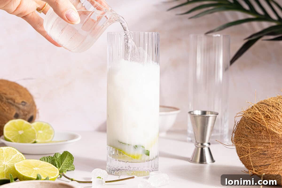 Club soda being gently poured into a coconut mojito, topping off the drink