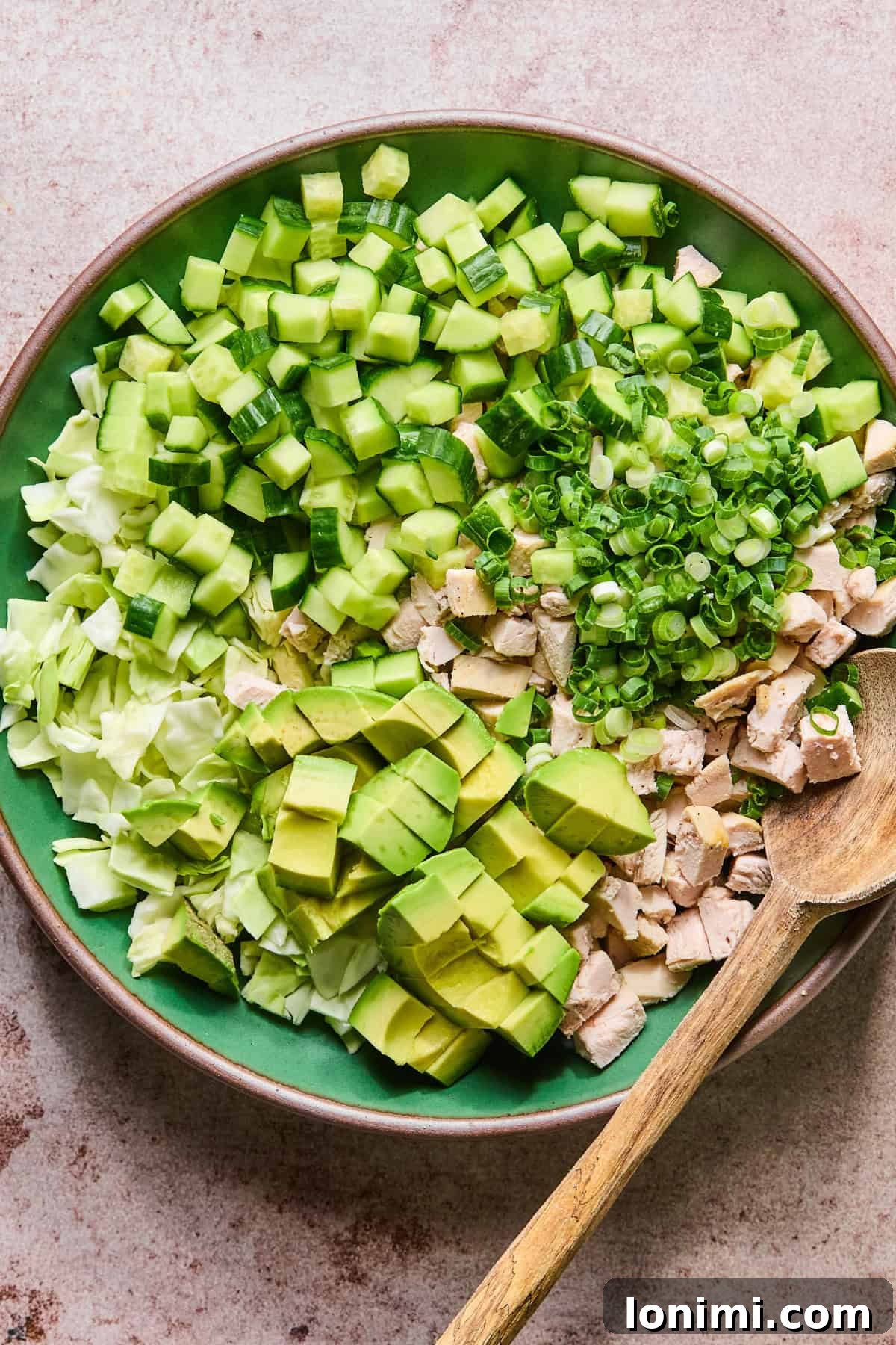A large mixing bowl filled with shredded chicken, chopped cabbage, diced cucumber, and green onions before the dressing is added.