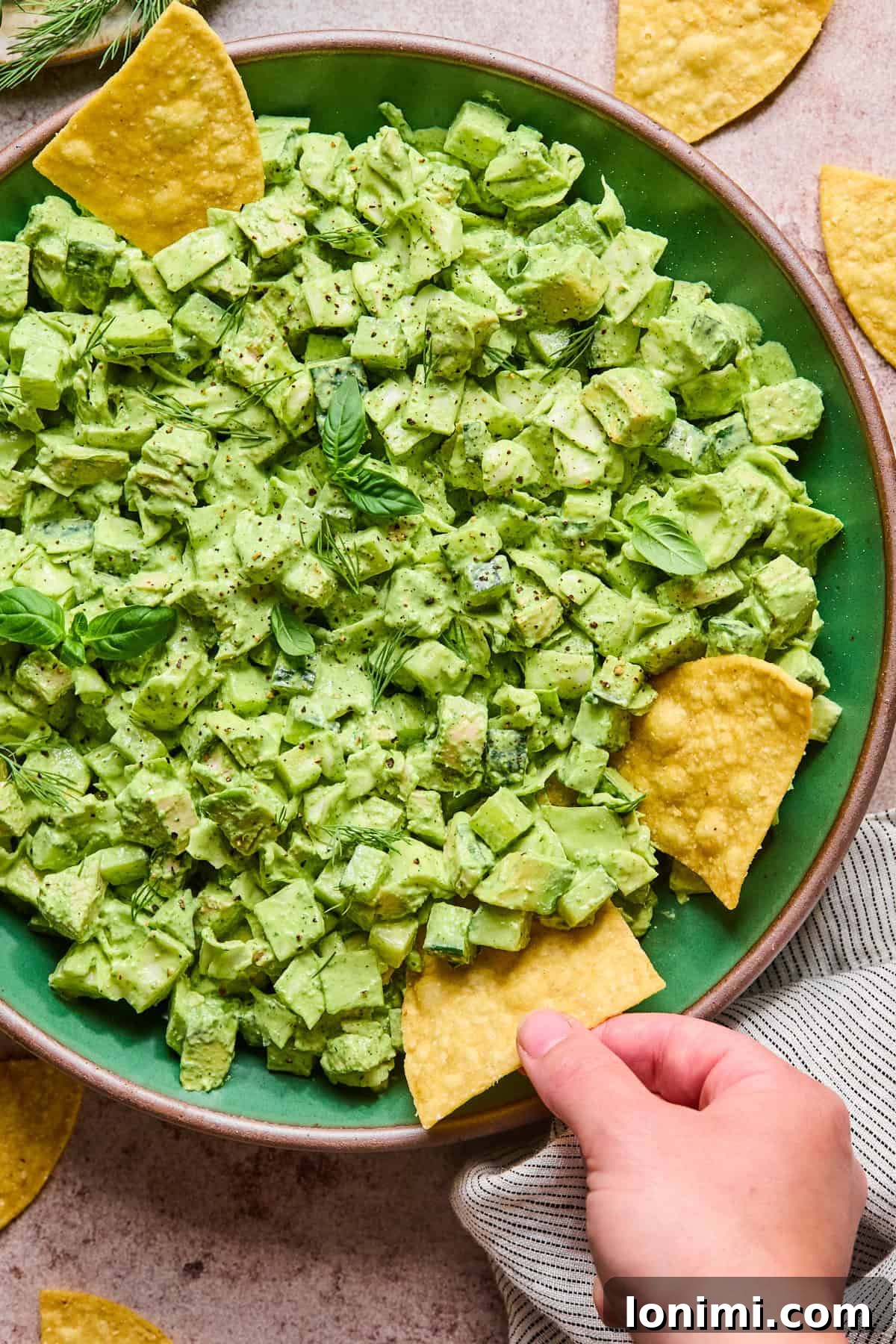A hand dipping a crispy tortilla chip into the bowl of green goddess chicken salad.
