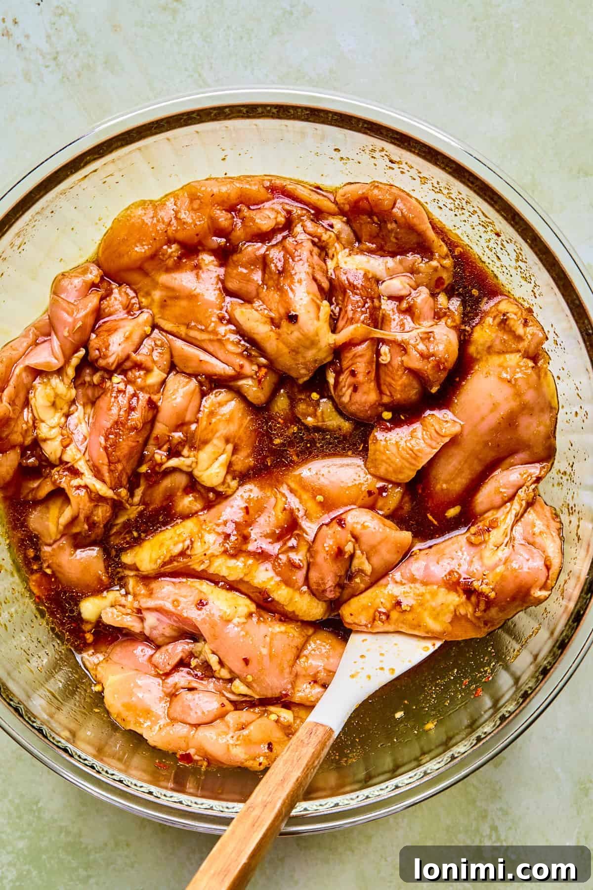 Raw chicken thighs in a glass bowl coated with marinade.