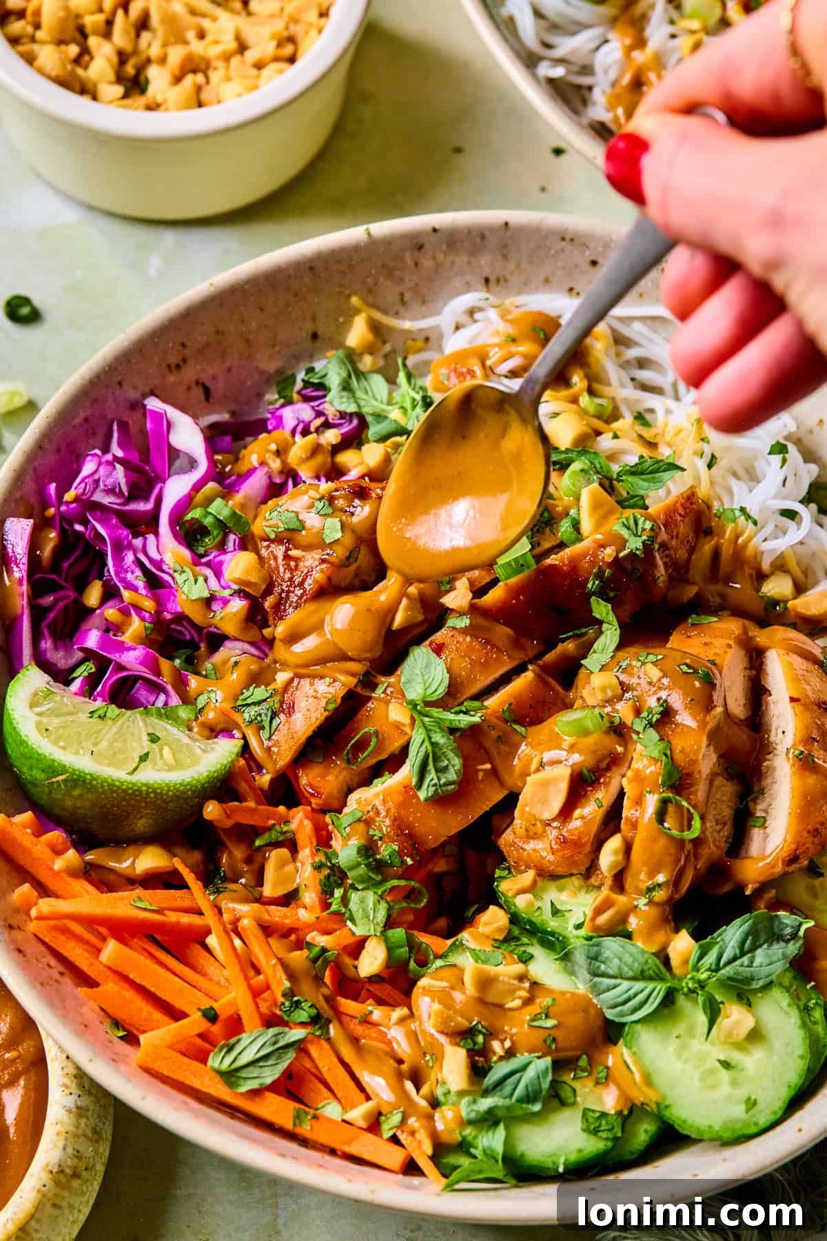 Spring roll bowls assembled with peanut dressing being drizzled over the top with a spoon.