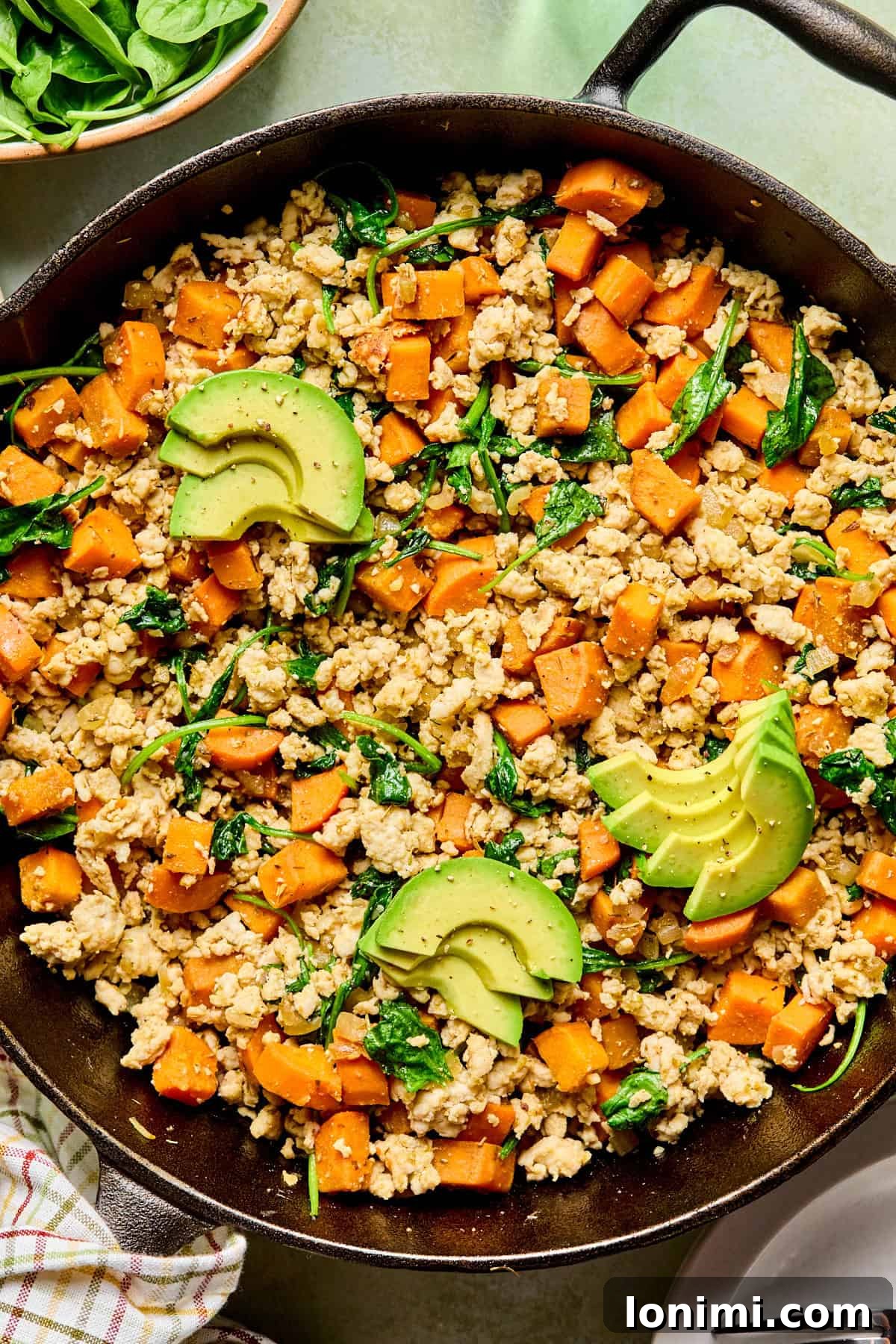 turkey sweet potato hash topped with avocado in a cast iron skillet