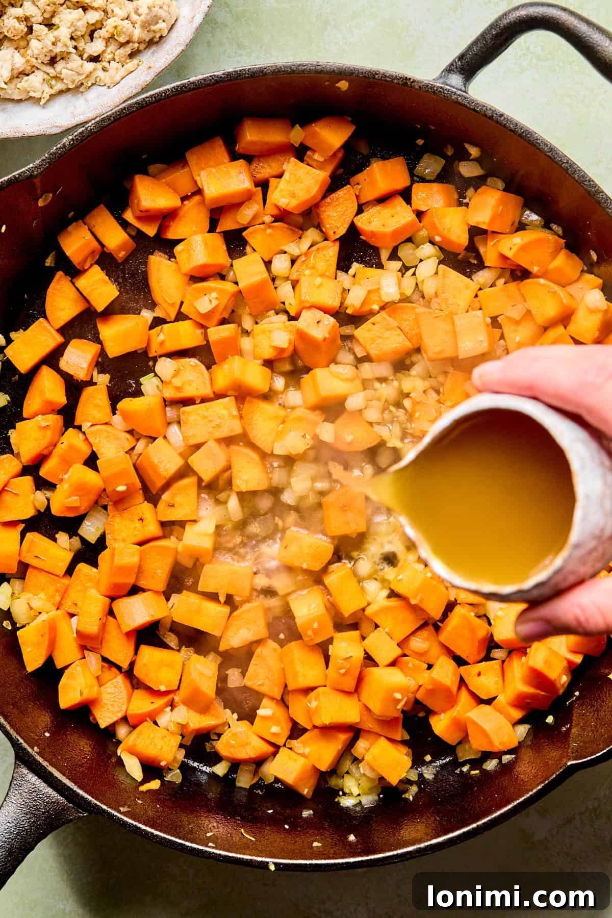 sweet potatoes in a skillet with broth being poured in