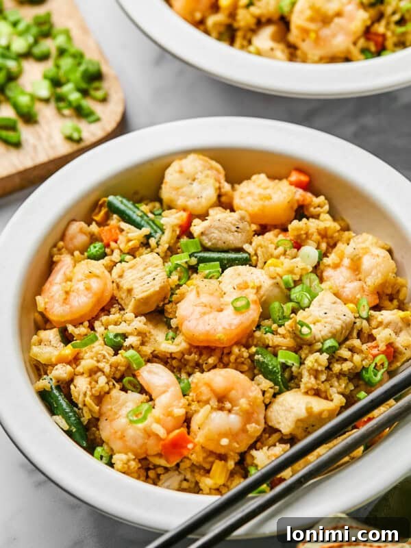 Chicken and shrimp fried rice in a white bowl with chopsticks