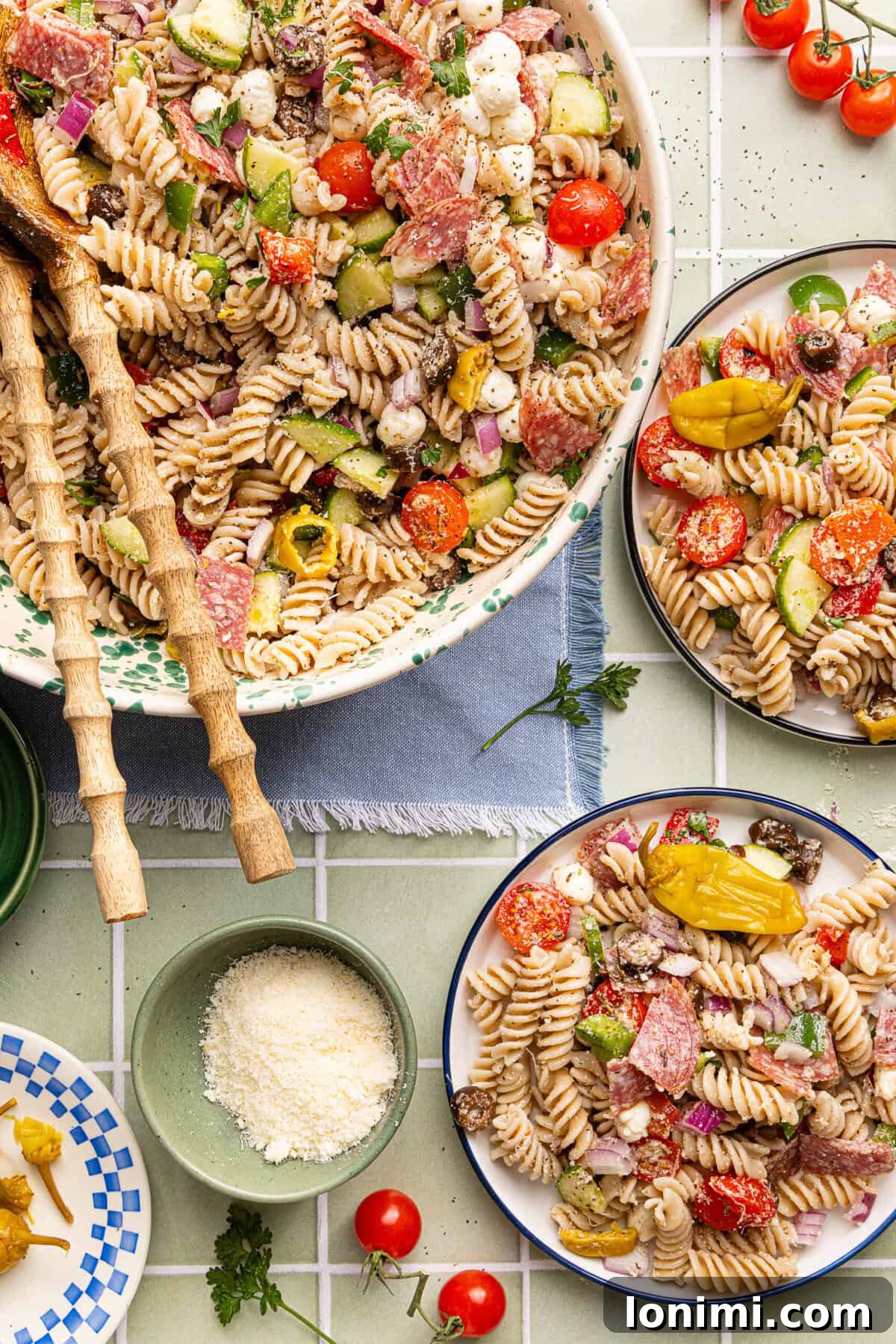 Gluten-Free Italian Pasta Salad Recipe for Delicious Summer Meals 2 Gluten free pasta salad served in a decorative bowl with wooden serving spoons, alongside two plates of pasta salad and a small bowl of grated parmesan cheese.